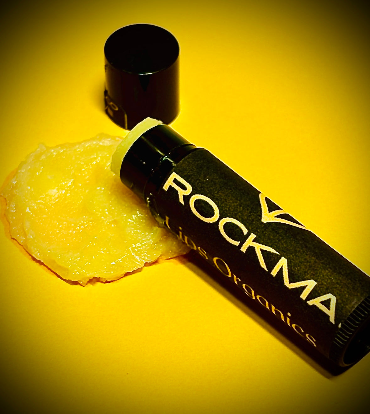 RockMa Lips Organcs lip balm on a yellow background with a smear of organic lip balm